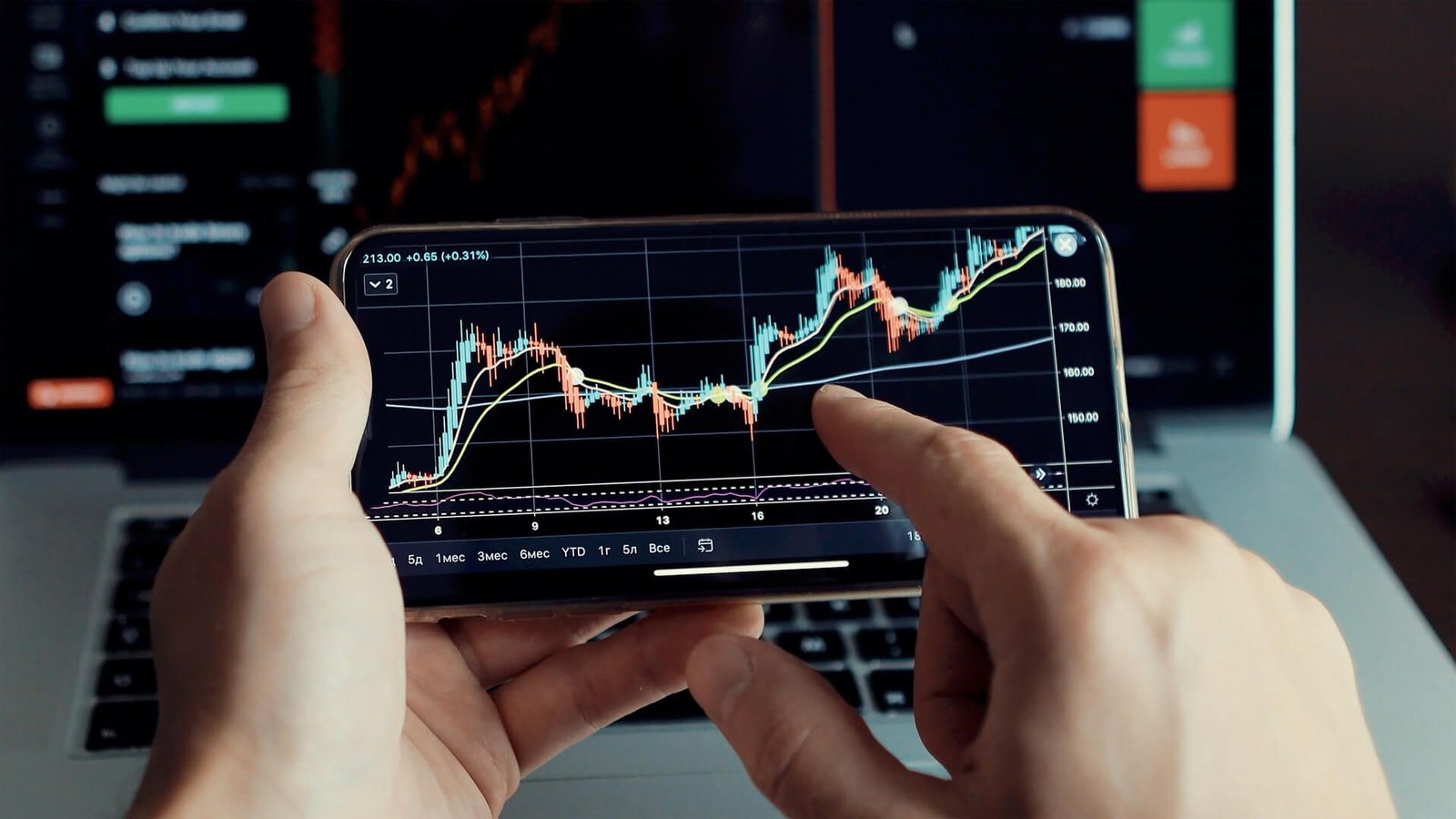 a man holding a phone which is showing trading graphs