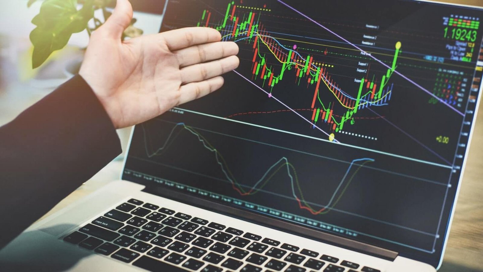 a man's hand pointing at a laptop showing a forex market graph