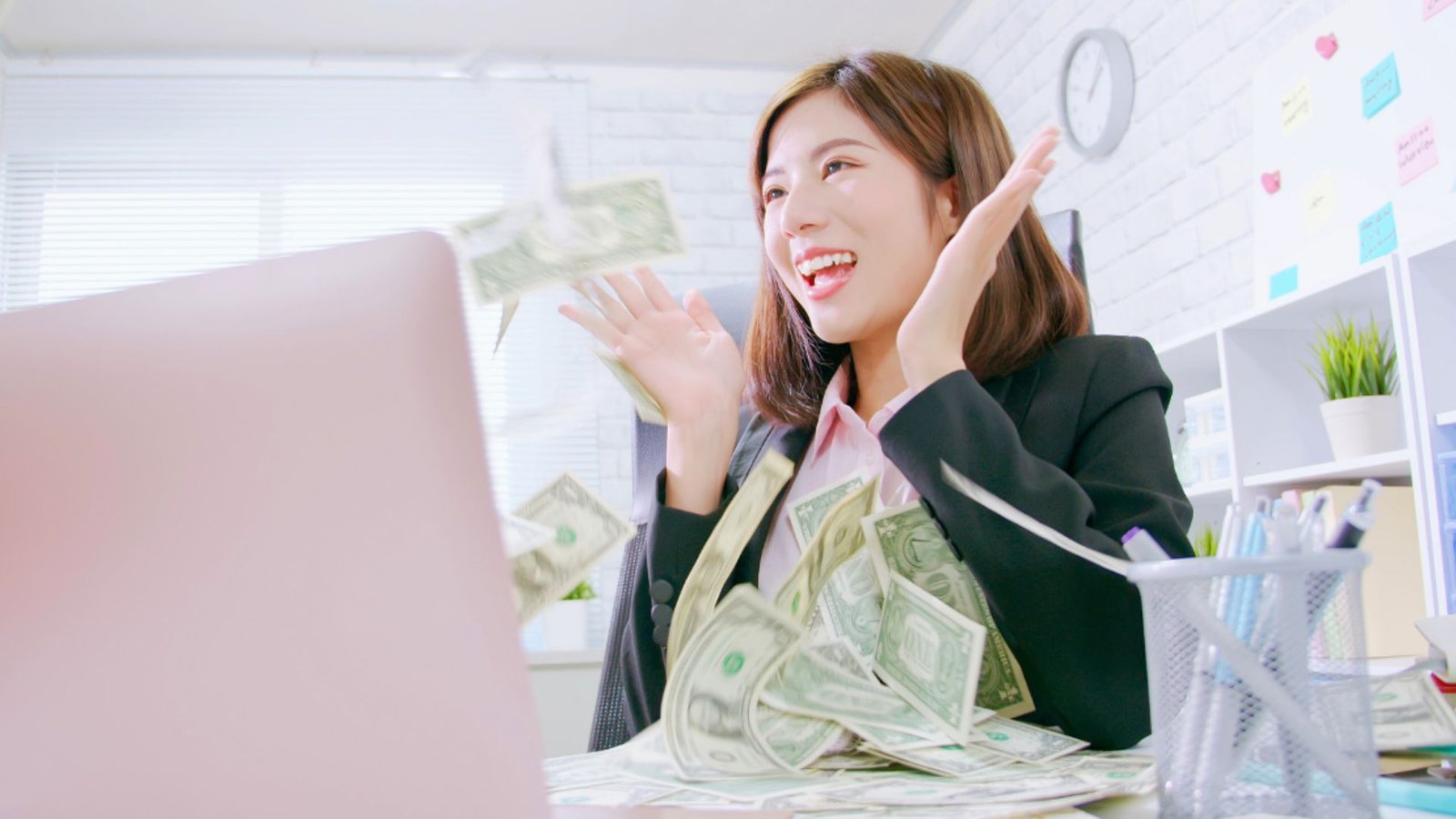 a lady looking happy with a laptop in her front and money